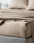 Taupe bamboo sheet set on a bed with matching pillowcases, shown in a softly lit bedroom setting.