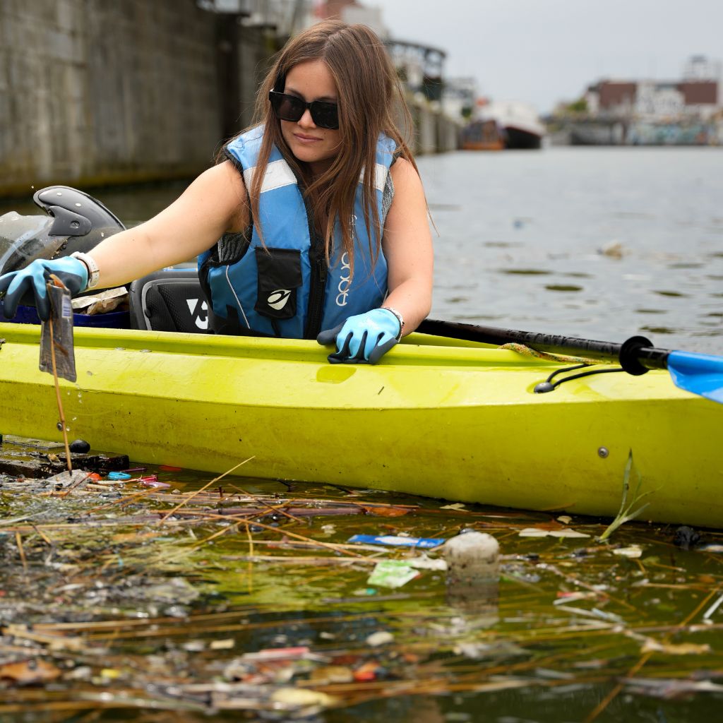 City to Ocean volunteer in a kayak cleaning up trash in a polluted body of water in Belgium
