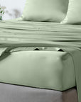 A bed dressed in a smooth, bamboo sage green sheet set with a fitted sheet and matching pillowcases, shown in a softly lit bedroom setting.