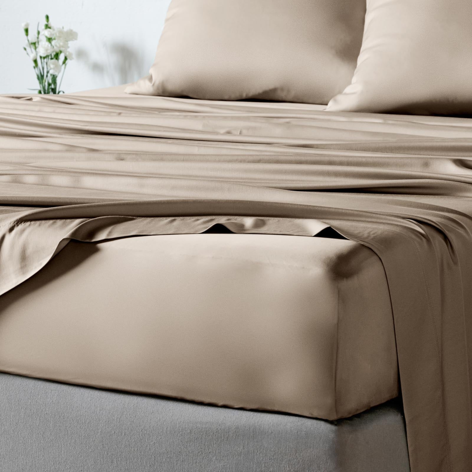 Taupe bamboo sheet set on a bed with matching pillowcases, shown in a softly lit bedroom setting.