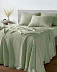A bed dressed in Bambaw Cozy sage bamboo flat sheet with matching fitted sheet and pillowcases