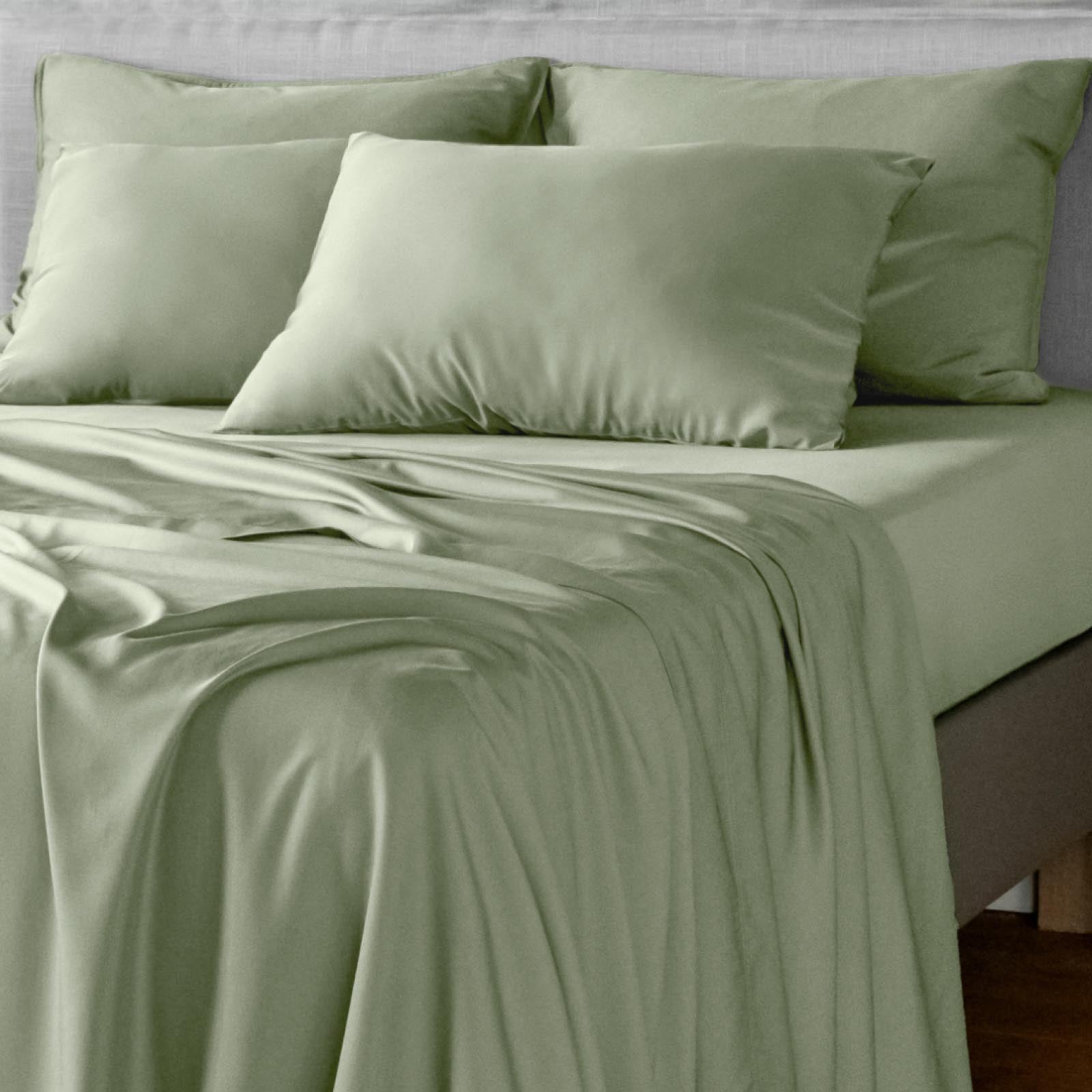 Light sage green bamboo bed sheets and matching pillowcases on a bed, shown in a clean, styled bedroom setting.
